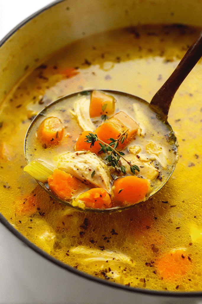 Golden turmeric chicken soup with carrots, celery, and tender chicken in a ladle for a warm anti-inflammatory meal