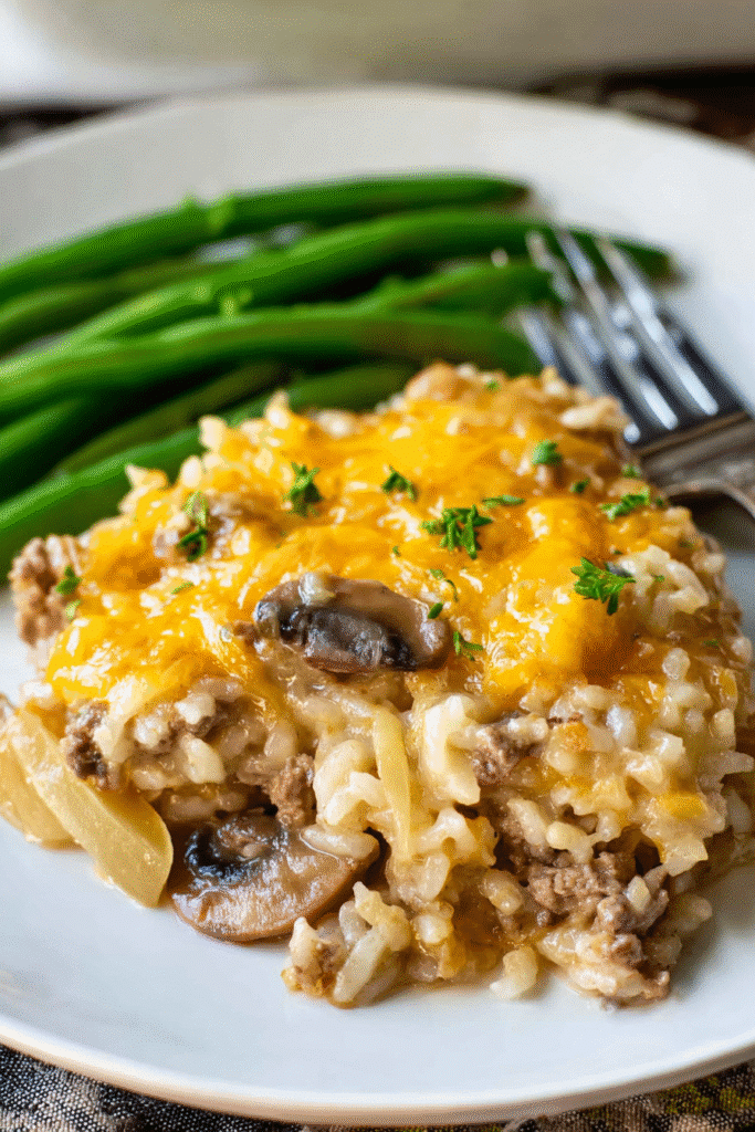 Cheesy hamburger rice casserole with mushrooms and onions topped with melted cheddar and served with green beans