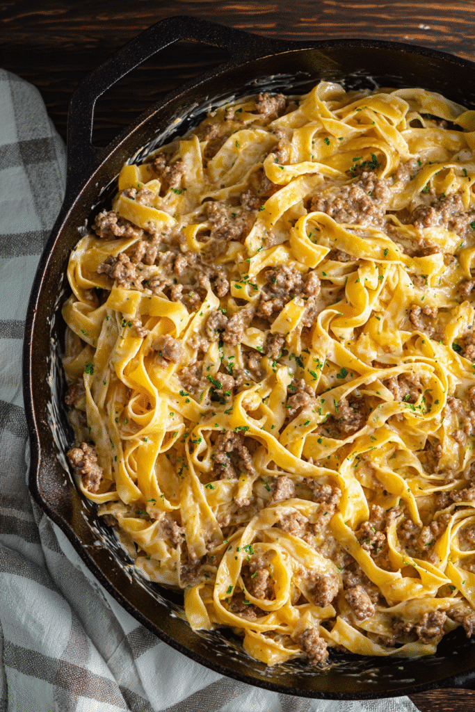 Creamy garlic butter pasta with ground beef and herbs served in a skillet, rich sauce coating each fettuccine strand perfectly