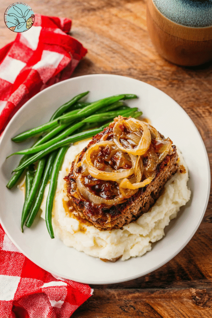 French onion meatloaf served over mashed potatoes with caramelized onions and green beans on a rustic wooden table