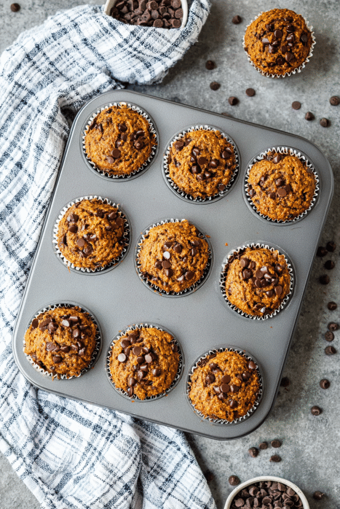 Freshly baked gluten-free keto pumpkin muffins with chocolate chips in a muffin tray, soft, moist, and perfectly golden