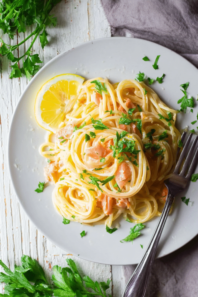Creamy smoked salmon carbonara pasta garnished with fresh parsley and lemon slice served on a white plate
