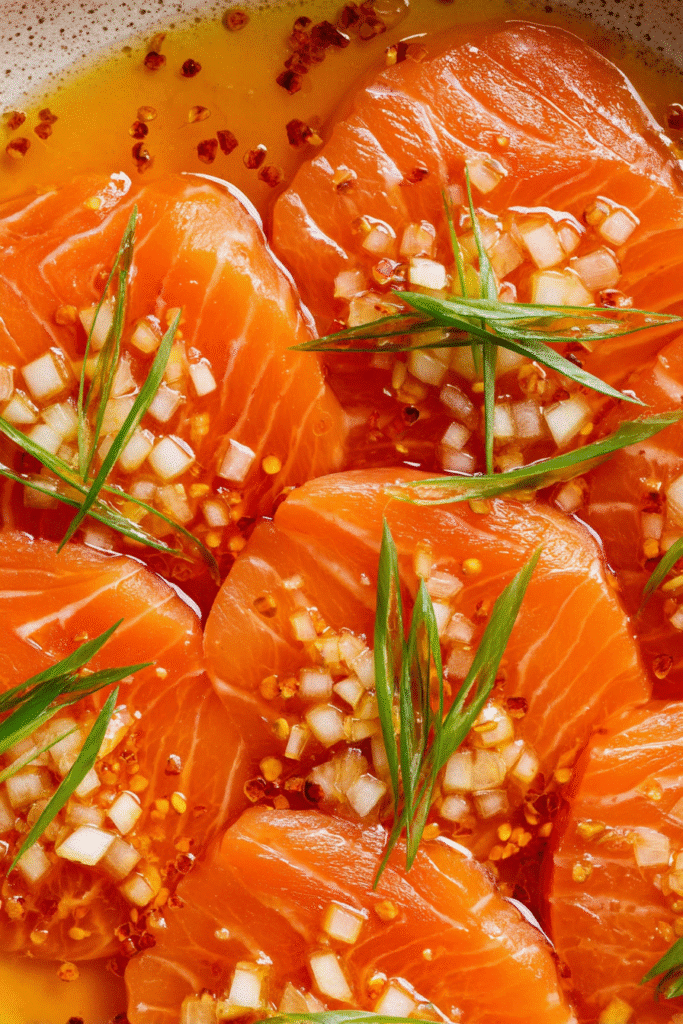 Close-up of soy citrus salmon sashimi with diced onions, chili flakes, and green herbs in a light tangy sauce